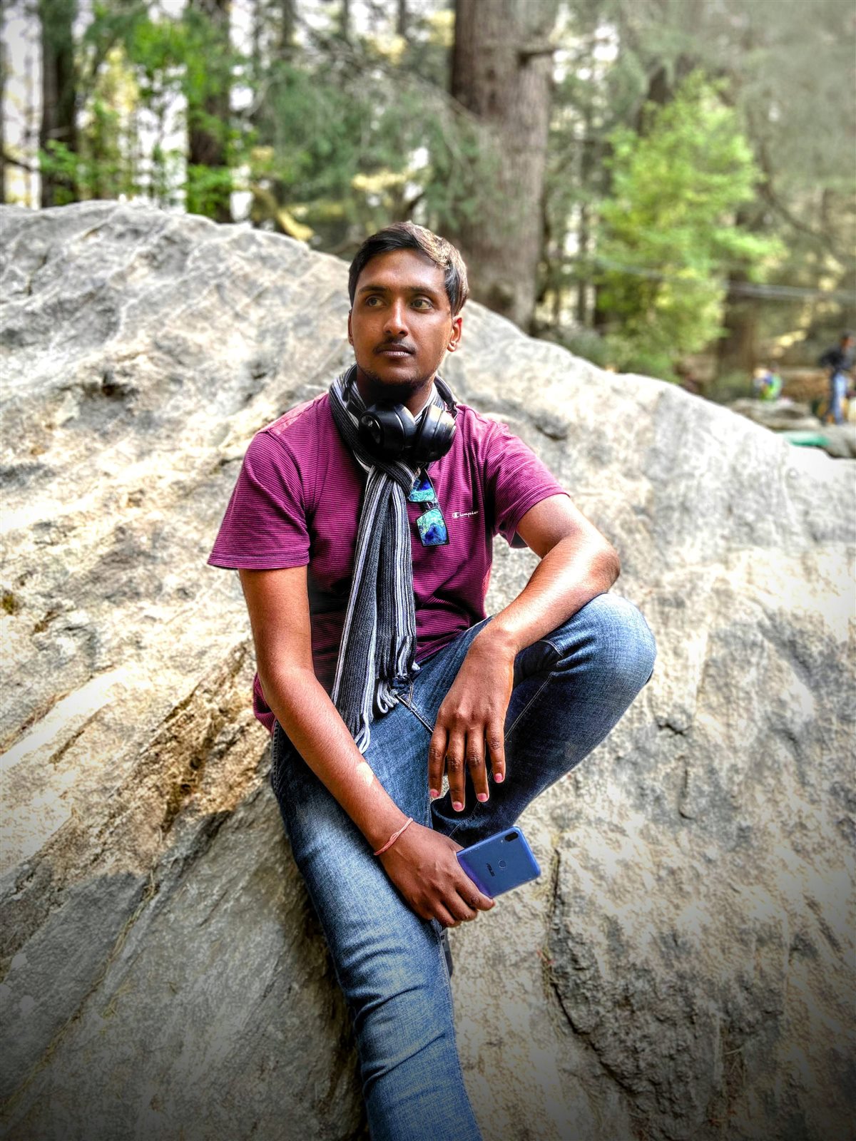 Vishwas Jha seated on a boulder in a pine forest, headphones round his neck